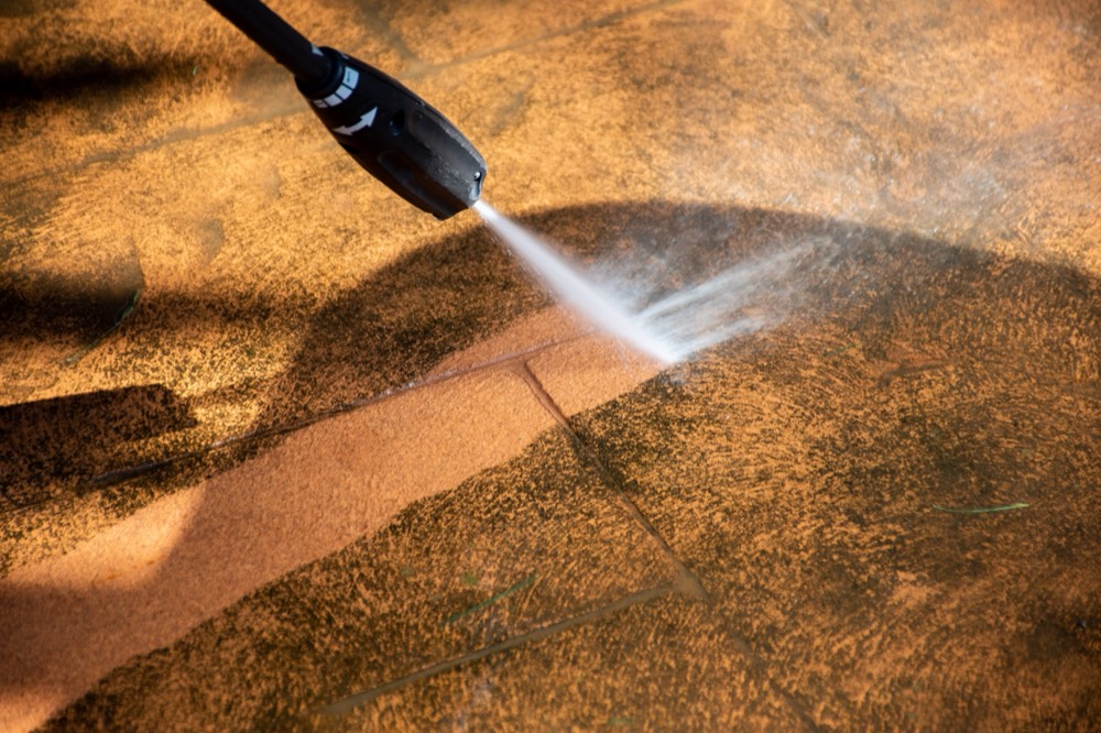 Pressure washing reveals a clean stripe on a patio tile surface